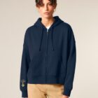 Veste sweat femme en coton biologique de couleur marine avec le logo de la marque sur la manche en sérigraphie doré.