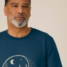 Tshirt homme manche courte coton biologique couleur bleu denim avec le dessin d'un yin et yang de la nature, d'un coté les montagnes et de l'autre la plage la sérigraphie est de couleur beige.
