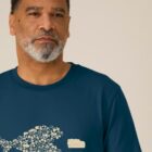 Tshirt homme manche courte coton biologique couleur bleu denim avec le dessin d'un poisson en forme de vélo qui mange un 4x4 avec une sérigraphie beige.