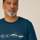 Tshirt homme manche courte en coton biologique de couleur bleu denim avec un dessin représentant les éléments de la nature sur une ligne avec l'inscription des racines aux étoiles la de sérigraphie est de couleur beige.