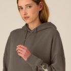 Sweat bio femme avec capuche de couleur mocha avec le dessin de la marque sur la manche représentant un homme qui grimpe sur un arbre au dessus de la planète. La couleur de sérigraphie est beige.