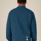 Sweat homme en coton biologique de couleur denim avec une sérigraphie beige en bas dans le dos représentant un arbre sur une planète.