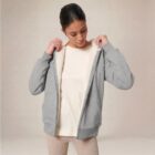Photo de présentation du sweat à capuche zippé unisexe Polaire, en coton biologique, coloris gris chiné, porté par un modèle femme. Collection Ardecho 07. Zoom sur la polaire.
