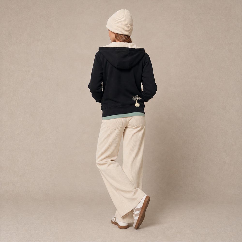 Photo de présentation du sweat à capuche zippé unisexe Polaire, en coton biologique, coloris noir, porté par un modèle femme. Collection Ardecho 07. Vue de dos avec le dessin de la marque en bas à droite, représentant un arbre sur la planète et un homme qui grimpe à l'arbre, la sérigraphie est de couleur beige.