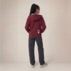 Photo de présentation du sweat à capuche unisexe Polaire, en coton biologique, coloris bordeaux, porté par un modèle femme. Collection Ardecho 07. Vue de dos avec le dessin de la marque en bas à droite, représentant un arbre sur la planète et un homme qui grimpe à l'arbre, la sérigraphie est de couleur beige.