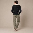 Photo de présentation du sweat à capuche zippé unisexe Polaire, en coton biologique, coloris noir, porté par un modèle homme. Collection Ardecho 07. Vue de dos avec le dessin de la marque en bas à droite, représentant un arbre sur la planète et un homme qui grimpe à l'arbre, la sérigraphie est de couleur beige.