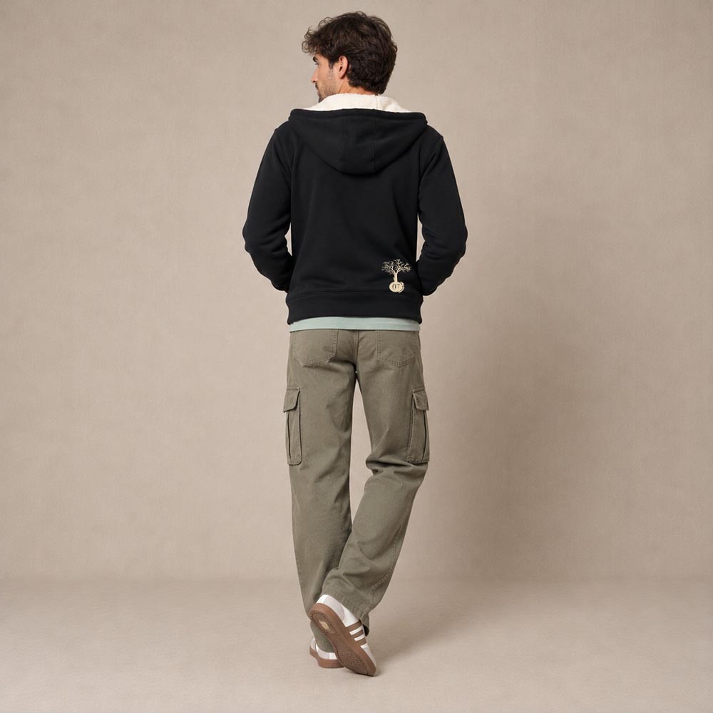 Photo de présentation du sweat à capuche zippé unisexe Polaire, en coton biologique, coloris noir, porté par un modèle homme. Collection Ardecho 07. Vue de dos avec le dessin de la marque en bas à droite, représentant un arbre sur la planète et un homme qui grimpe à l'arbre, la sérigraphie est de couleur beige.