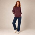 Sweat femme à capuche en coton biologique couleur aubergine avec le dessin du logo de la marque qui représente un arbre sur une planète et une personne qui monte à l'arbre. Poche kangourou, le dessin est sur la manche de couleur beige.