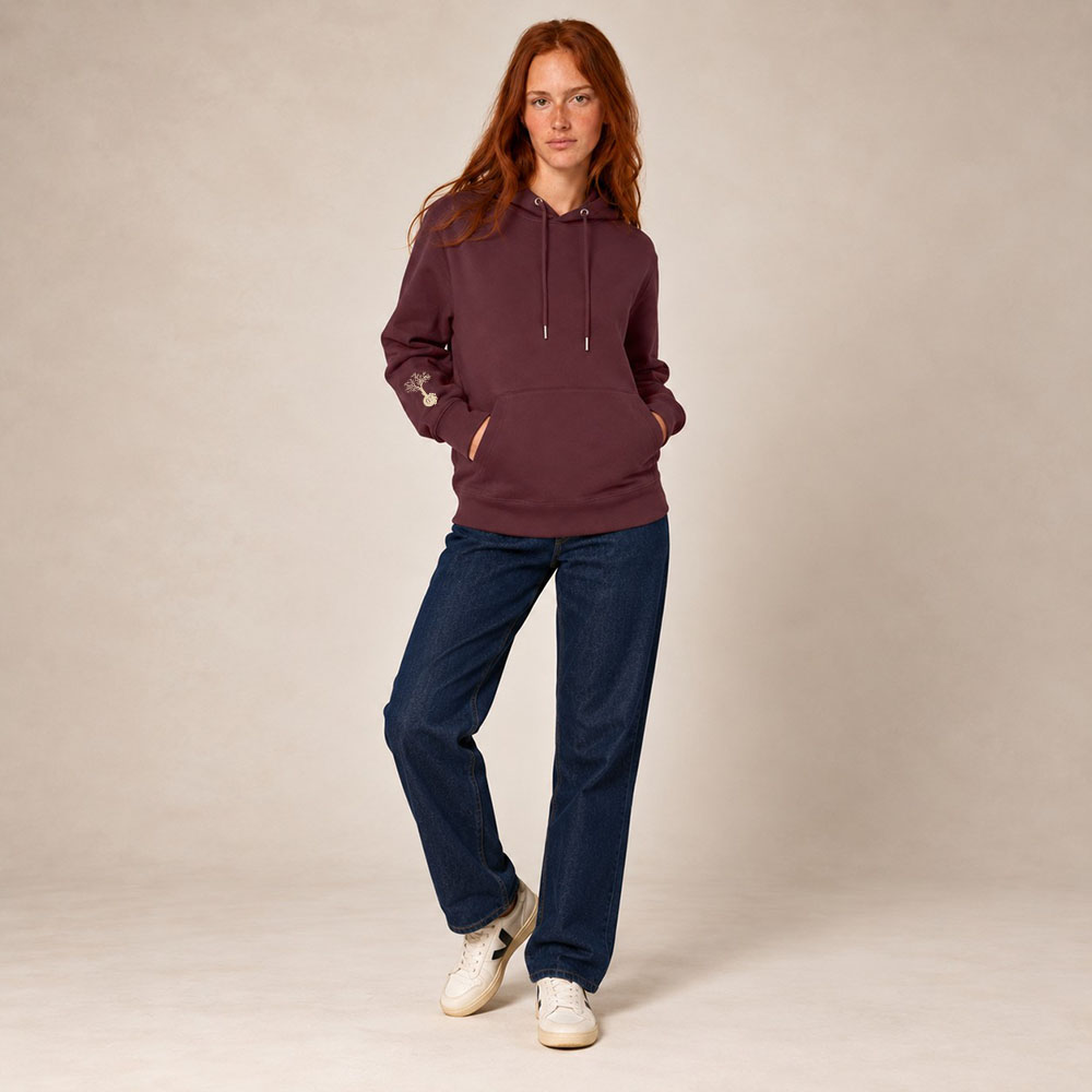 Sweat femme à capuche en coton biologique couleur aubergine avec le dessin du logo de la marque qui représente un arbre sur une planète et une personne qui monte à l'arbre. Poche kangourou, le dessin est sur la manche de couleur beige.