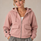 Sweat coton bio femme avec une capuche couleur rosé et une fermeture éclaire. Vue de face. Dessin de la marque sur la manche de couleur noir, représentant un arbre sur la planète et une personne qui grimpe à l'arbre. Zoom sur la veste.