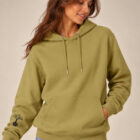Sweat femme à capuche en coton biologique couleur olive avec le dessin du logo de la marque qui représente un arbre sur une planète et une personne qui monte à l'arbre. Poche kangourou, le dessin est sur la manche de couleur noir. Zoom sur le sweat.