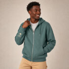Sweat avec capuche et fermeture éclaire pour homme en coton biologique de couleur vert jade. Le logo de la marque est imprimé en beige sur la manche, un arbre sur une planète et un homme qui monte à l'arbre. Zoom sur la veste.