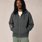 Sweat avec capuche et fermeture éclaire pour homme en coton biologique de couleur anthracite. Le logo de la marque est imprimé en beige sur la manche, un arbre sur une planète et un homme qui monte à l'arbre. Zoom sur la veste.