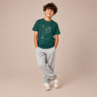 T-shirt enfant manche courte en coton biologique de couleur vert sapin avec un dessin représentant des planètes en forme de ballons tenu par le petit prince et son renard. La couleur de sérigraphie est beige.