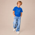 T-shirt enfant manche courte en coton biologique de couleur bleu roi avec un dessin représentant des planètes en forme de ballons tenu par le petit prince et son renard. La couleur de sérigraphie est beige.