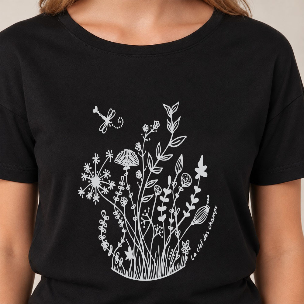 T-shirt femme à manche courte en coton biologique couleur noir avec un dessin de bouquet de fleurs en forme allongée. Avec une inscription ' La clef des champs', la sérigraphie est de couleur argenté. Zoom sur le t-shirt.